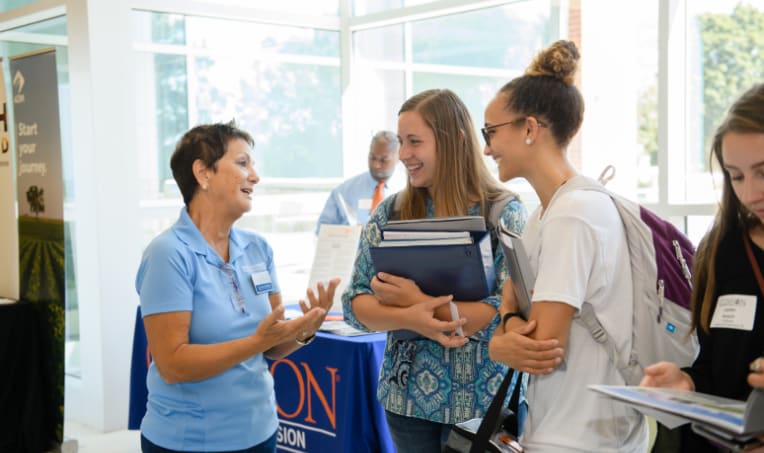 Female students talk with a middle-aged female employee during a job fair in Littlejohn Coliseum.