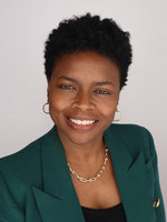 Professional headshot of a smiling Black woman with short, curly hair, wearing a green blazer and gold earrings.