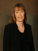 Professional headshot of a woman with long hair wearing a black jacket over a polka dot blouse.