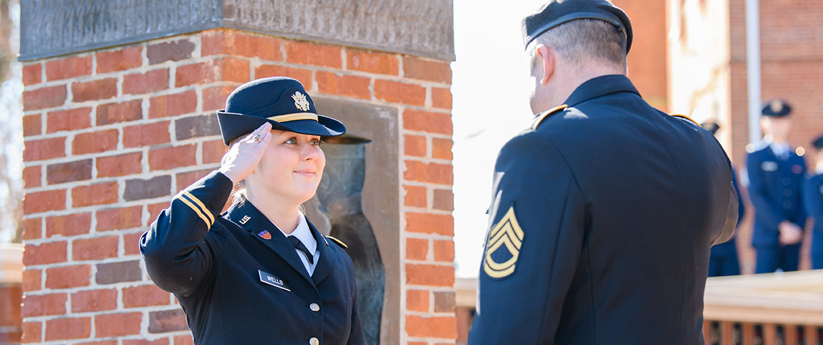 Man and woman in Army dress uniform facing each other and saluting one another.