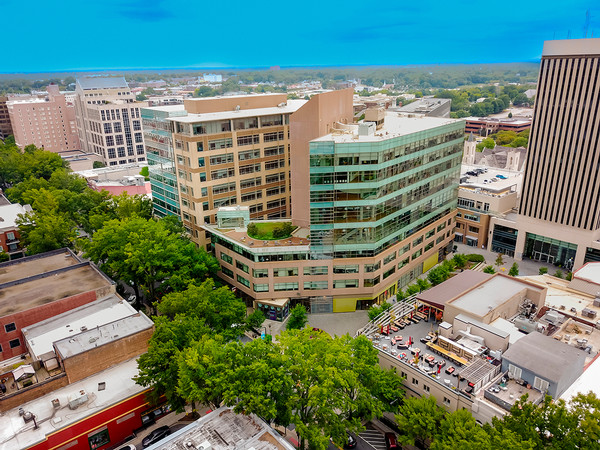 Aerial view of a modern multi-story building surrounded by urban greenery and nearby city structures.