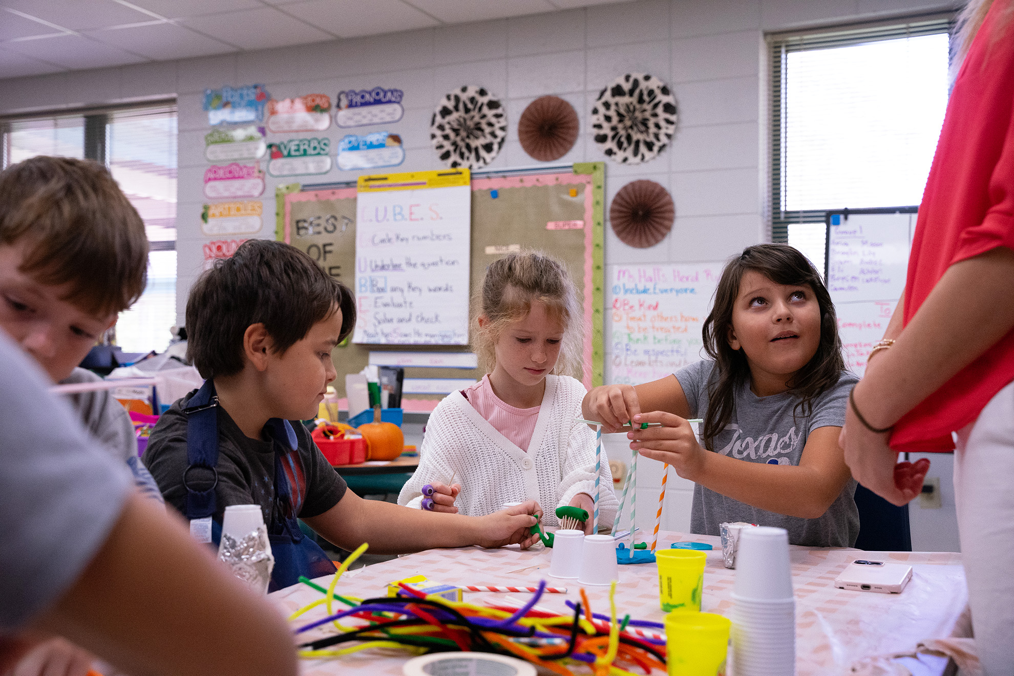Children engaged in a hands-on activity, using colorful materials at a classroom table.