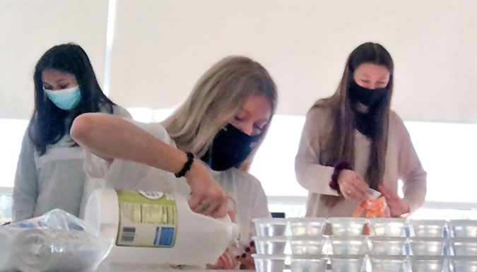 Three female students, masked, working in a lab with chemicals.