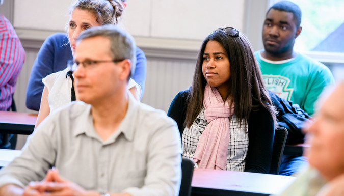 adults of various ages sit in a classroom setting, all looking in the same direction