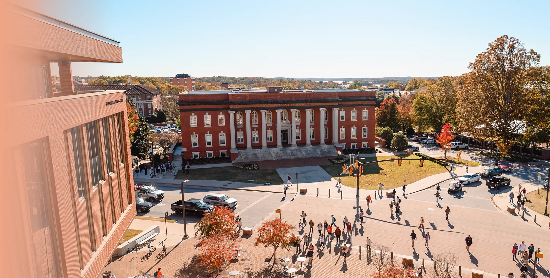 A top down view of a busy intersection is filled with students on their way to class. A greek revival style building and view of a lake and mountains are seen off in the distance.