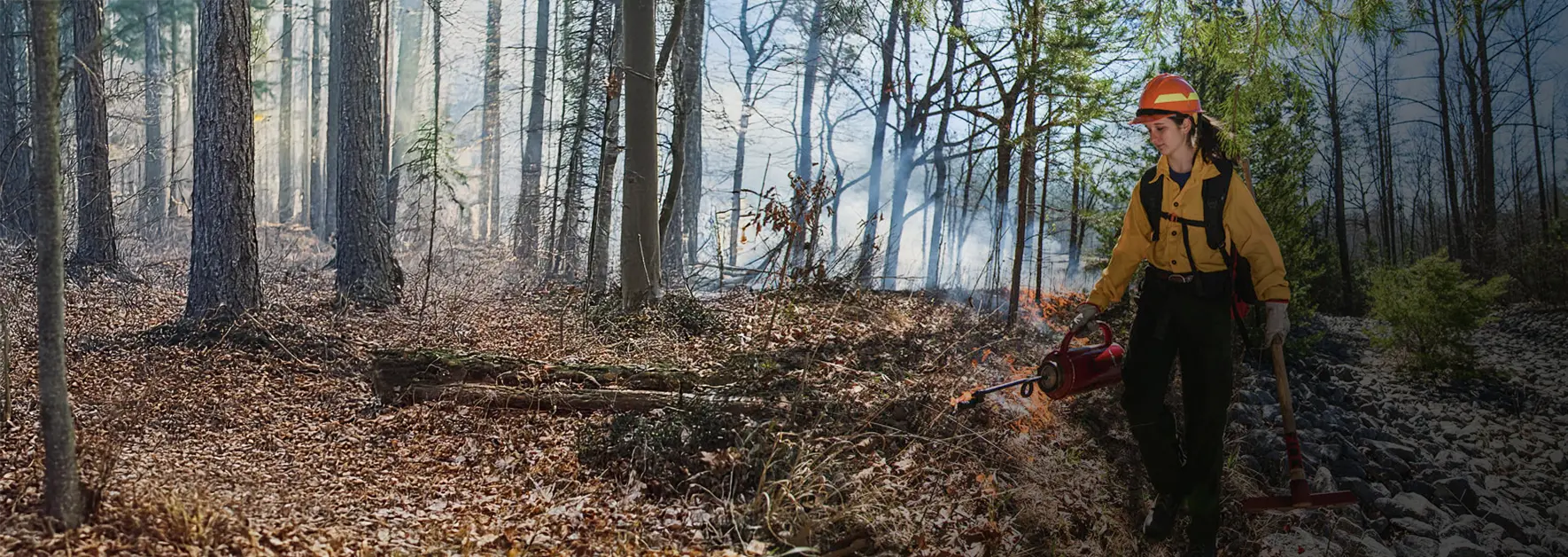 A female student in fire safety equipment uses a kerosine torch to start controlled burn