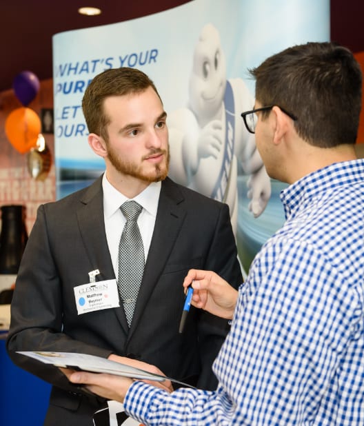 Male Clemson engineering student in professional attire speaks with Michelin representative at the career fair.