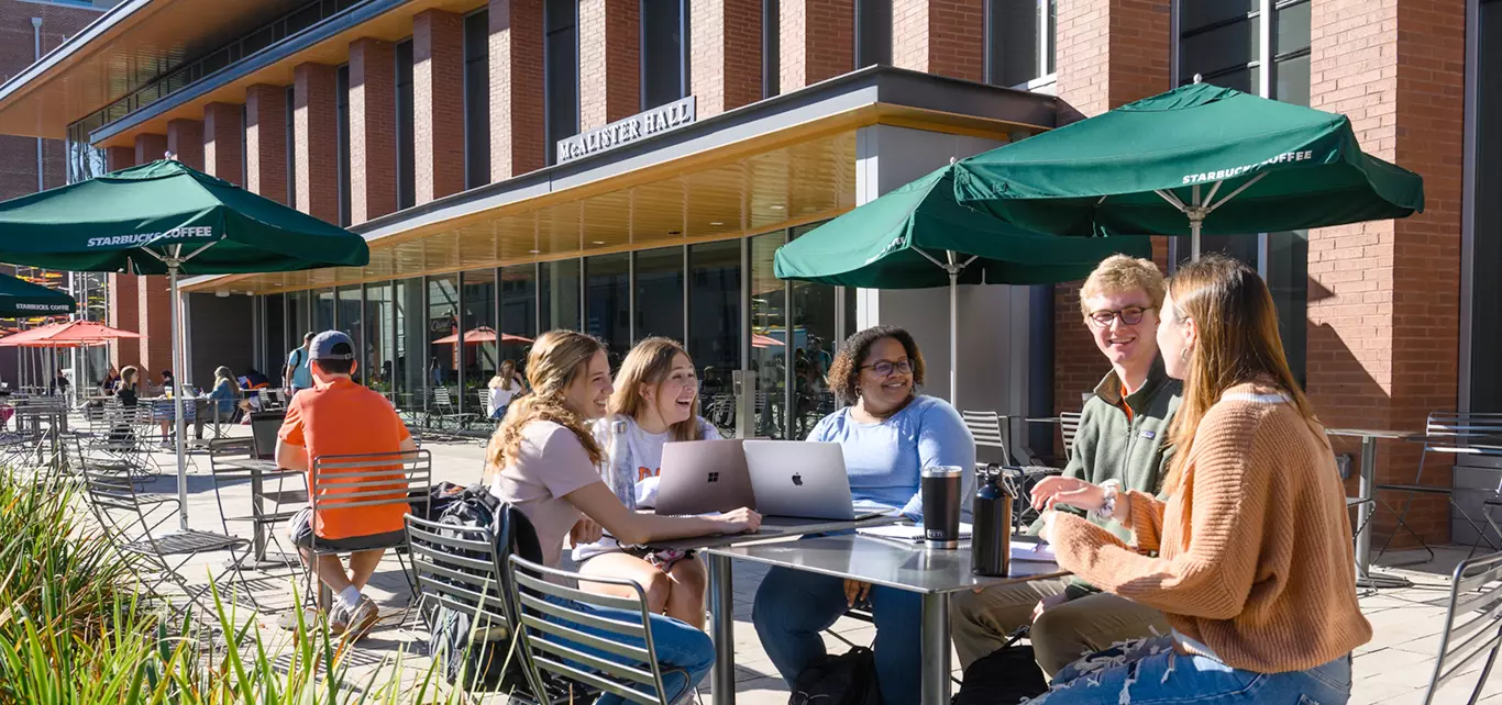 A group of student talk and study together outside of the campus dining hall