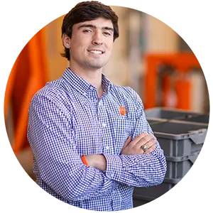 A male student wearing a purple gingham dress-shirt poses in a warehouse.