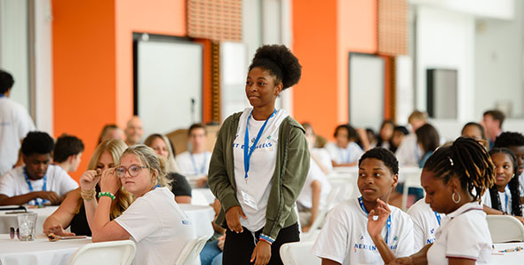 A smiling female student stands while her peers look on.