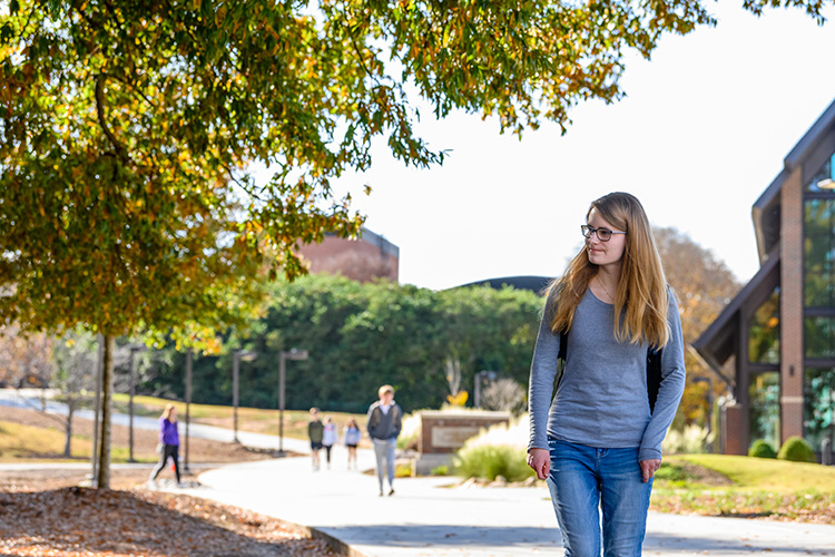 A female student walks the sidewalk infront of the Samuel Caden Chappel at dusk