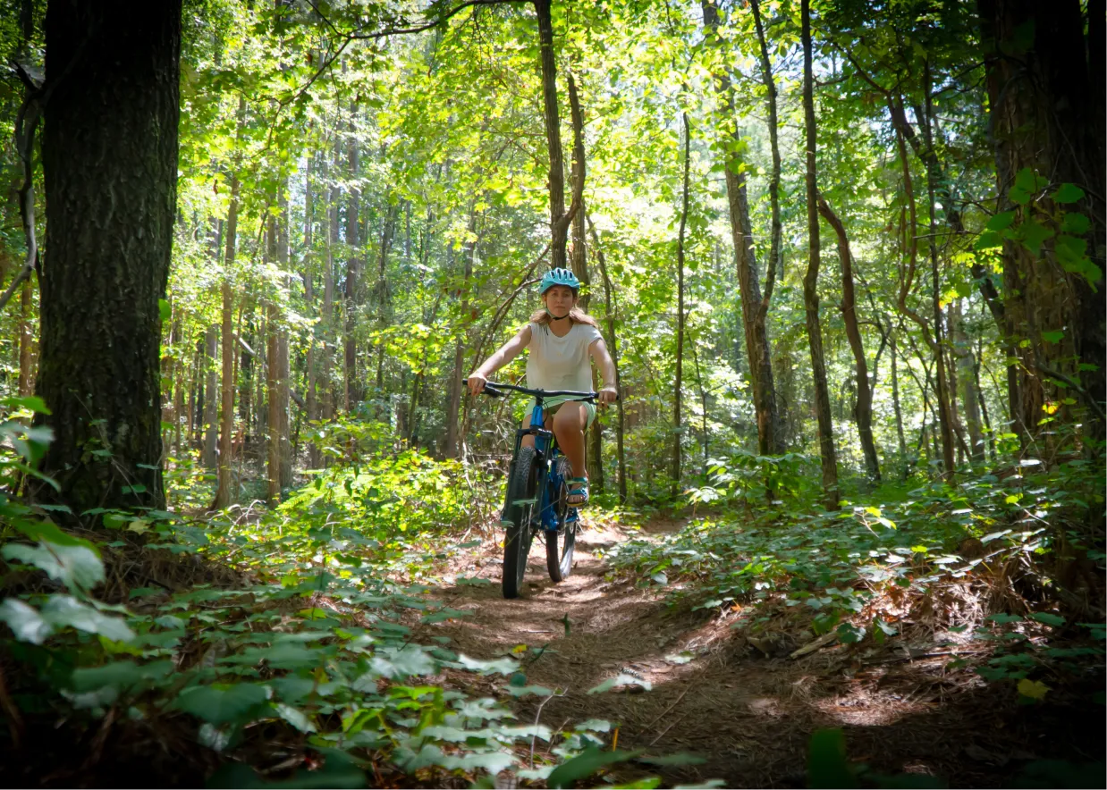 A female college student mountain bikes on a wooded trail.