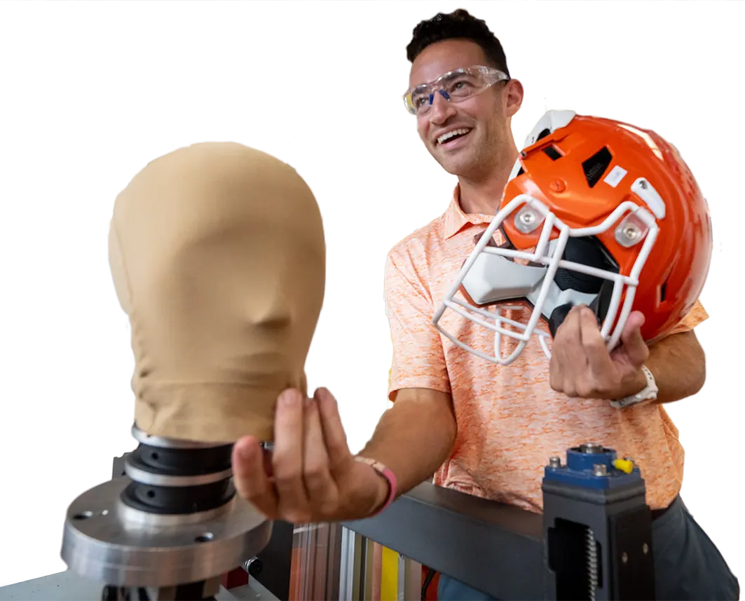 A male researcher holds a clemson football helmet as he prepares to perform tests using a stuffed mannequin head