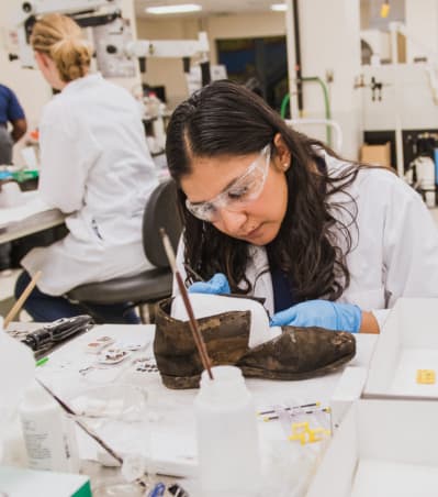 Female student in lab examines a historic shoe.