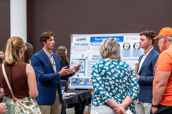 Two male bioengineering students present their capstone project findings to a group of onlookers