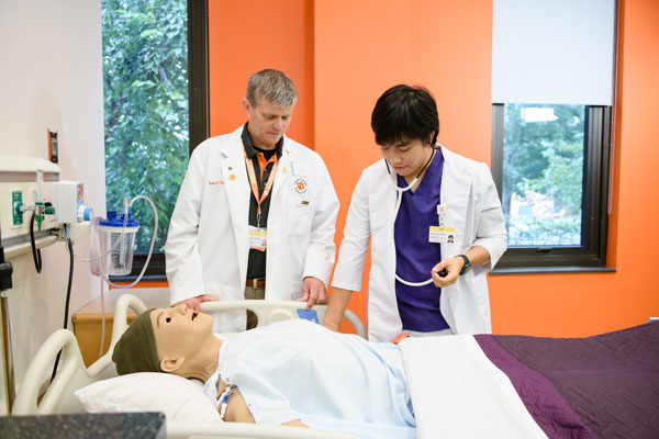 a student and faculty member examine a simulation dummy in the nursing sim lab