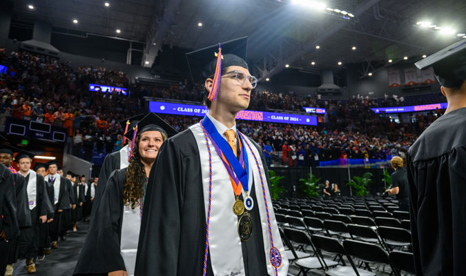 A student walks at graduation wearing a Phi Kappa Phi medal