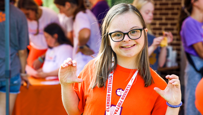 female ClemsonLIFE smiling at the camera presenting her hands in the shapes of the letter c