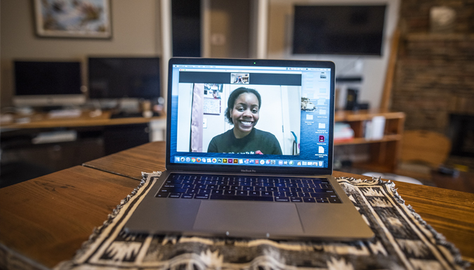 an open computer on a table in a home setting, with screen showing a smiling african american female 