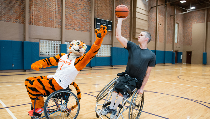 tiger mascot and man in wheelchairs on a basketball court shooting and blocking baskets