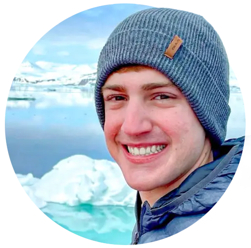 A male student wearing a winter hat and jacket poses in front of glacial ice and water.