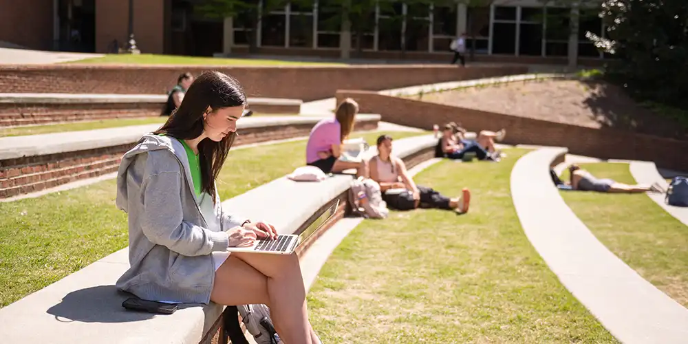 A student sits on their laptop outdoors at the amphitheater.