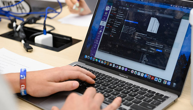 Students hands hover over a laptop keyboard.