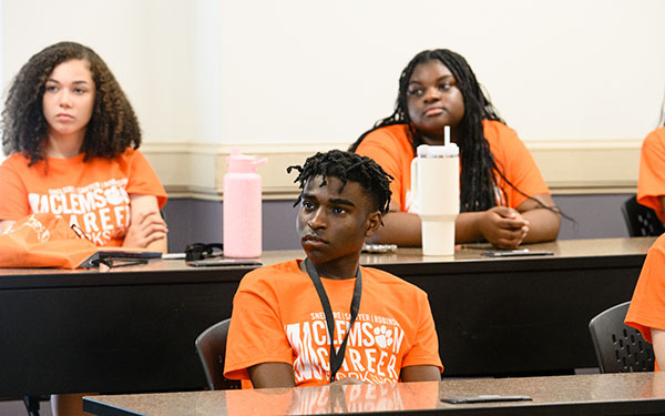 Students participating in a career workshop, wearing orange t-shirts, attentively listening during a session.