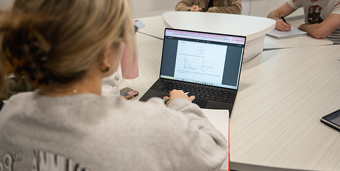 Student working on math problems on a laptop during a study session in a collaborative setting.