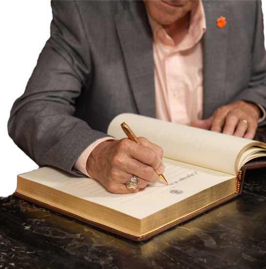 A man in a business suit signs a large book. 