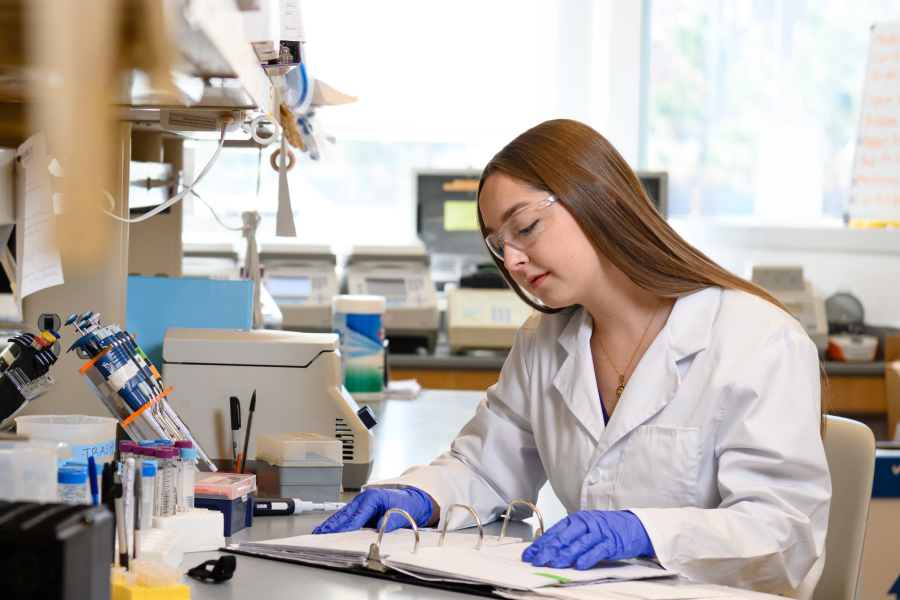 Elizabeth Caldwell reads notes in her science lab while wearing protective glasses, gloves and a lab coat. 