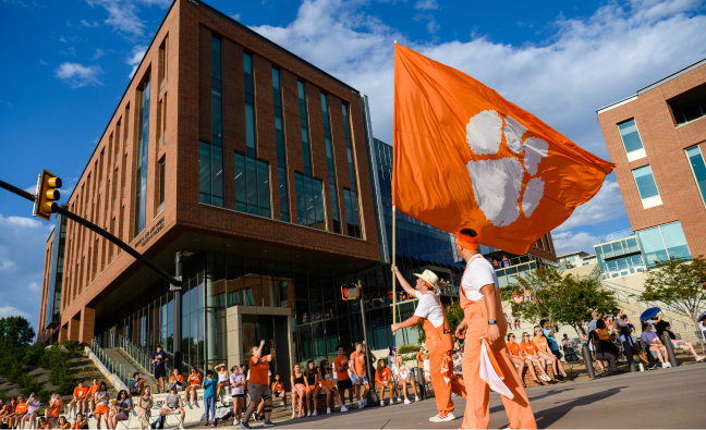 Students in orange overalls wave large orange flags during the First Friday parade.