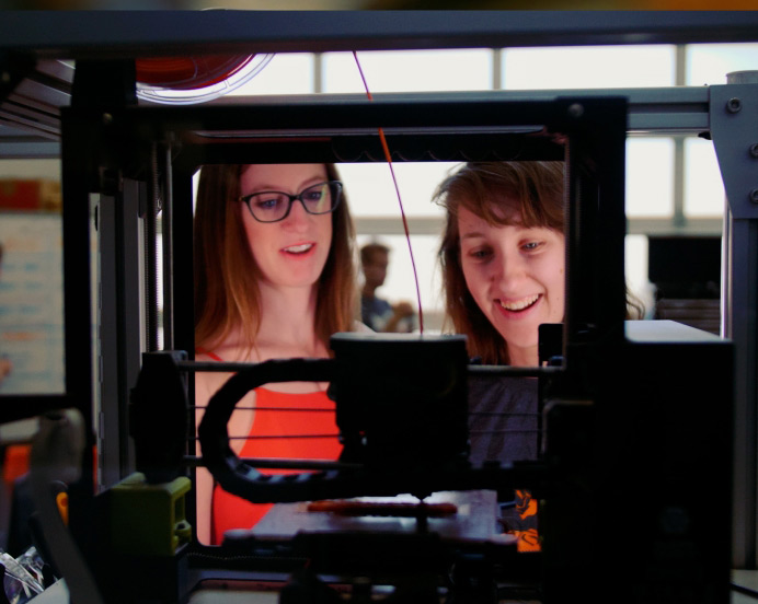 two students looking at a 3-d printer working