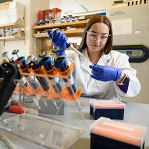 A woman wearing lab gear fills vials with a syringe.