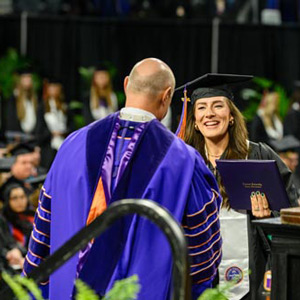 President Jim Clements handing a woman her diploma during a graduation ceremony.