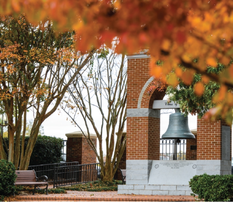 The Old Tillman Hall Bell in the Carillon Garden peeks through a covering of orange and red-colored trees.