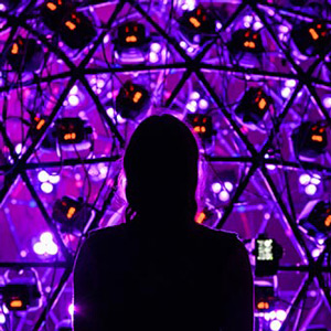 The siloutte of a person stands in front of a collection of purple stage lights.