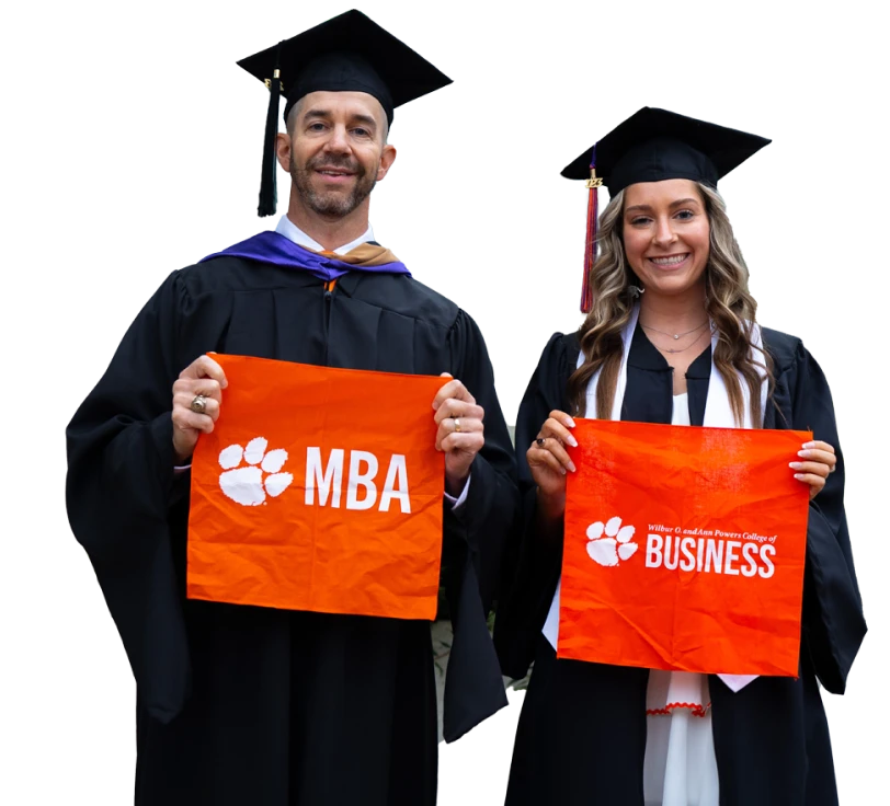 Two students stand next to each other wearing their cap and gowns while holding orange tiger rags that have "MBA" and "Wilbur O. Ann Powers College of Business" on them.