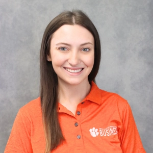 Headshot of a young woman smiling in an orange polo shirt with the word "Business" printed on it.