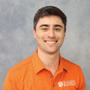 Smiling man wearing an orange polo shirt with "Clemson Business" logo.