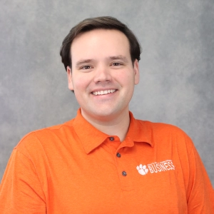 Smiling professional wearing an orange polo shirt with a "Business" logo on it.