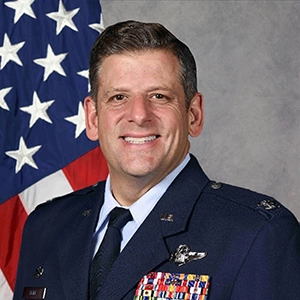 Portrait of a military officer in uniform, standing in front of an American flag, showcasing their medals.