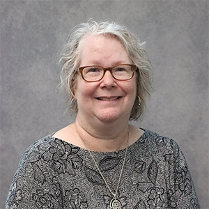 A smiling woman with glasses and curly hair, wearing a floral-patterned top.