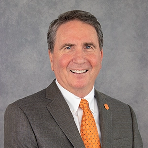 Professional headshot of a smiling man in a suit and tie with an orange tie.