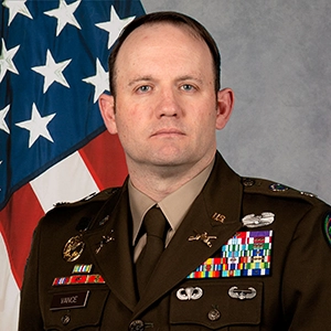 Portrait of a military officer in uniform, standing in front of an American flag, showcasing their medals.