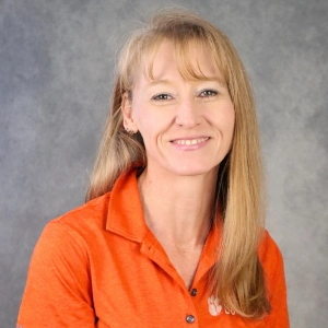 A smiling woman wearing an orange polo shirt with a Clemson University logo.