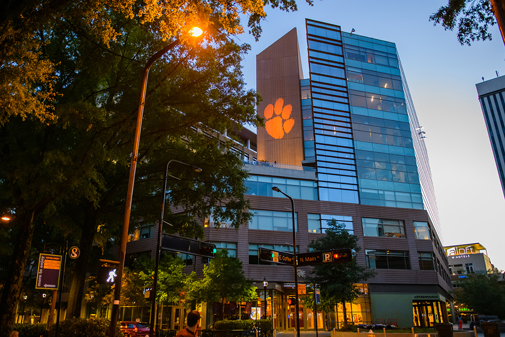 A modern building at dusk, featuring a large illuminated Clemson University paw print on its facade.
