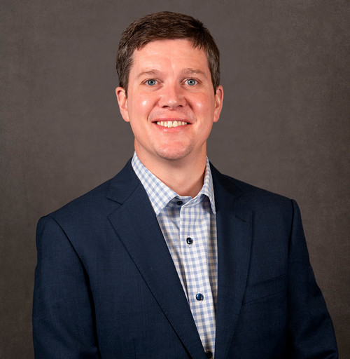 Man with short brown hair wearing white shirt and navy jacket.