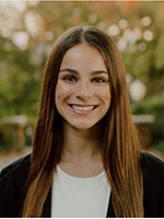 A smiling young woman with long hair poses outdoors, showcasing a friendly and approachable demeanor.