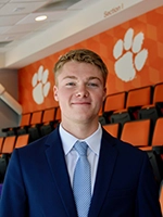 Young man in a suit stands confidently in front of an orange and white paw print backdrop.